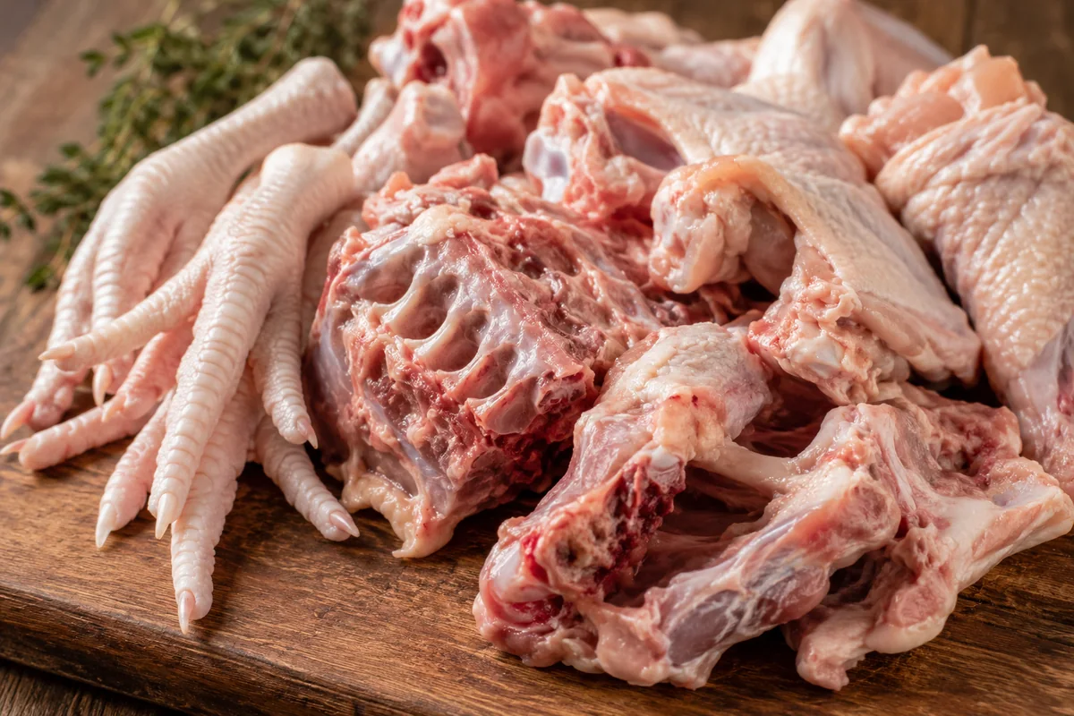 Choosing the right bones for chicken stock Close-up of raw chicken bones, backs, wings and feet, on a board, the collagen-rich parts for making chicken stock