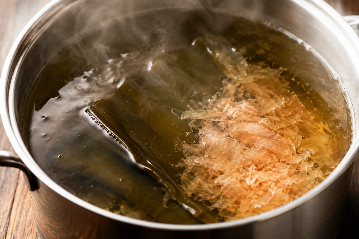 Close-up of dashi broth simmering with kombu and bonito flakes, the savory base at the heart of miso soup
