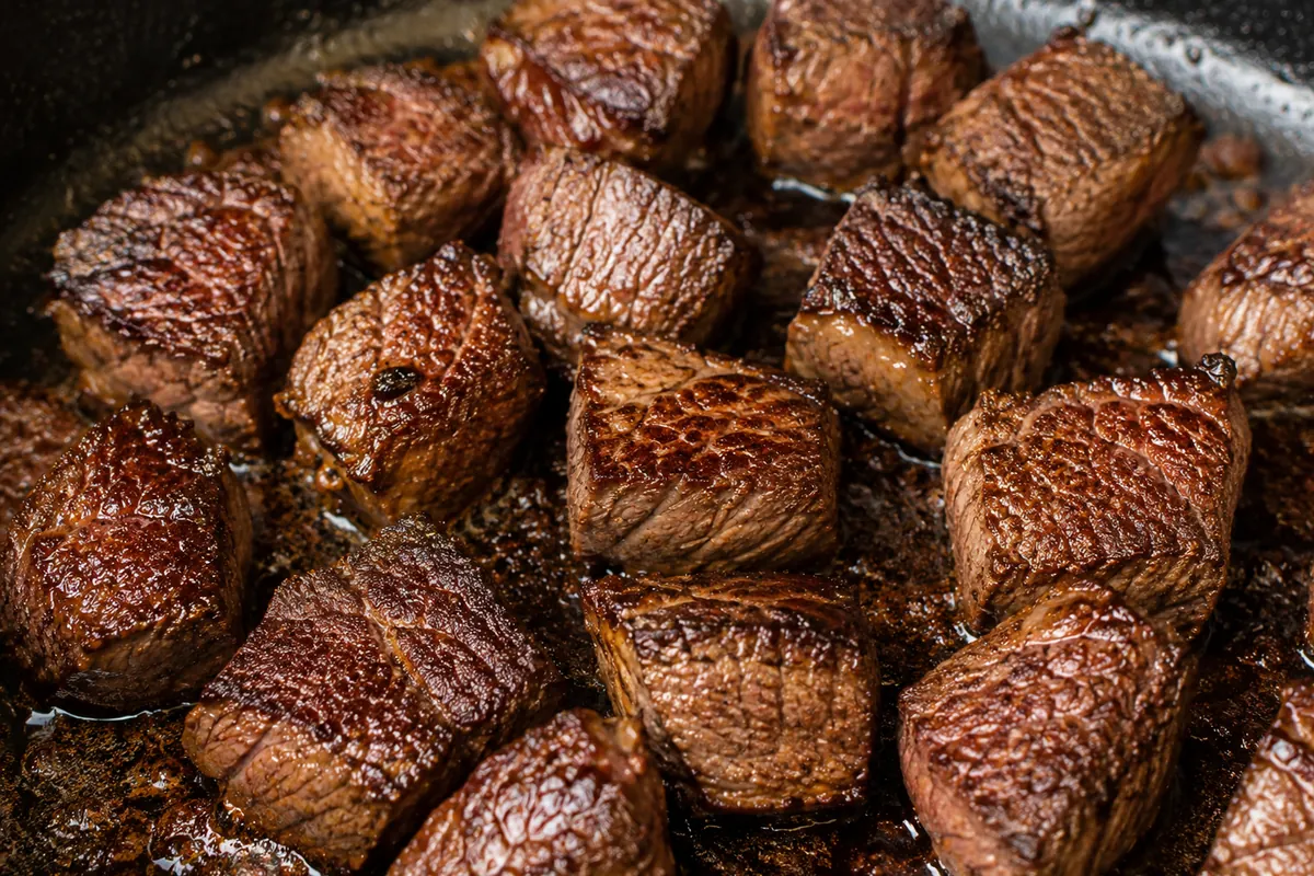 Why searing the beef first matters for stew Close-up of cubes of beef searing to a deep brown crust in a hot skillet, the first step before the slow cooker